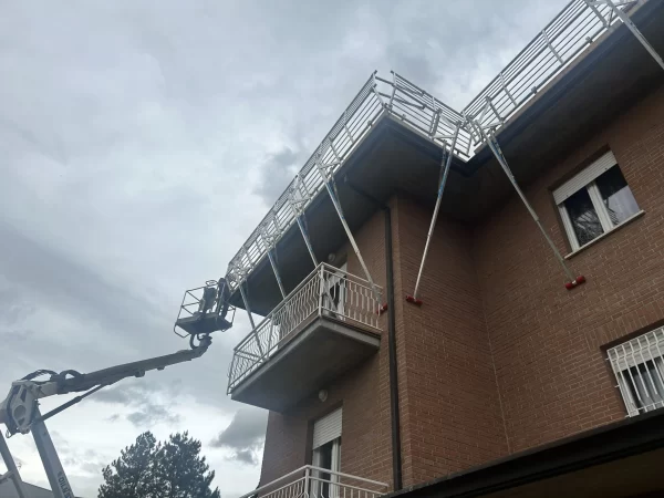 Operatore su piattaforma aerea installa parapetti SGS su tetto di edificio in mattoni